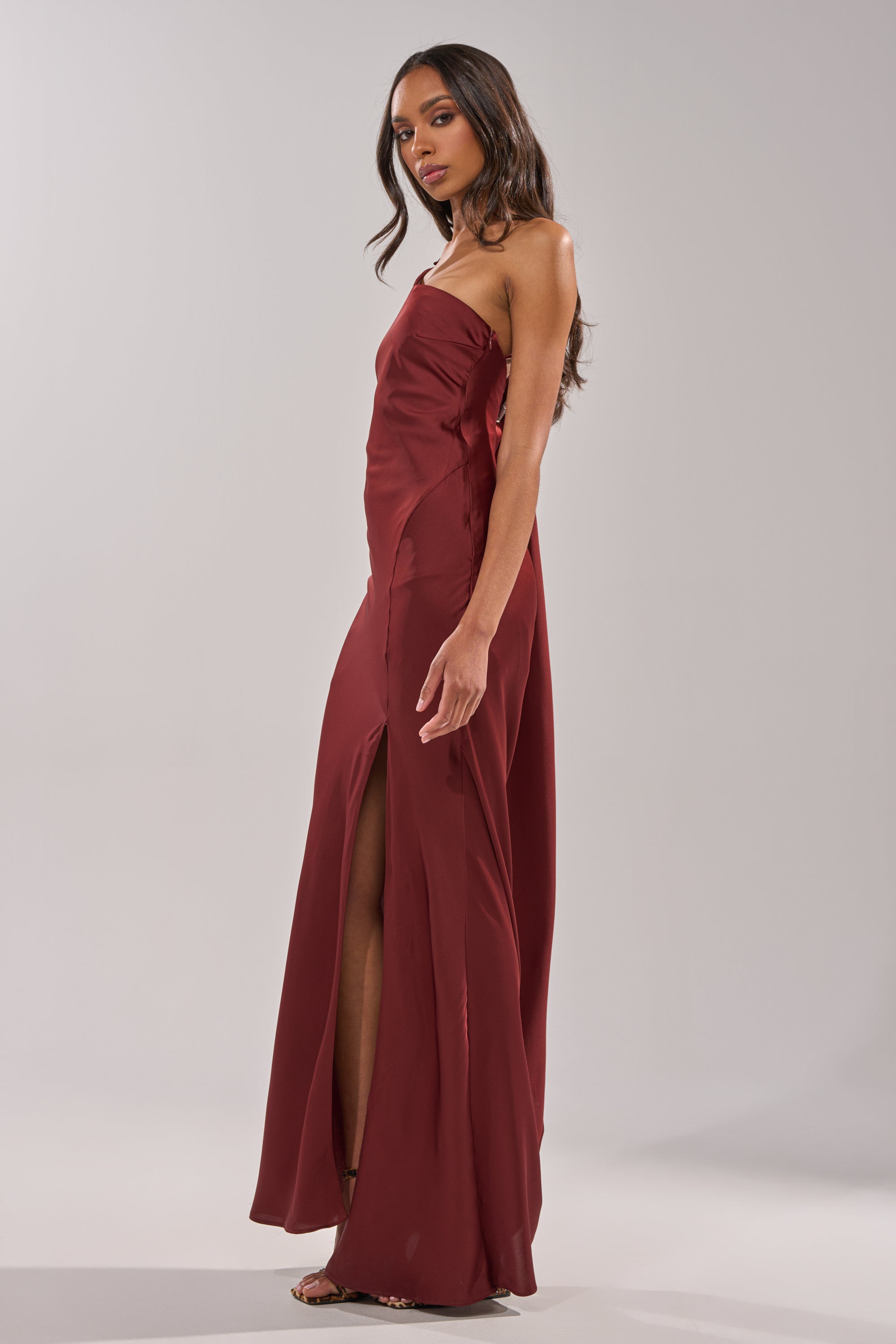 A woman confidently stands in heels against a plain light background, wearing the RSVP READY SATIN MAXI DRESS—a strapless satin maxi dress with a high side slit. 3
