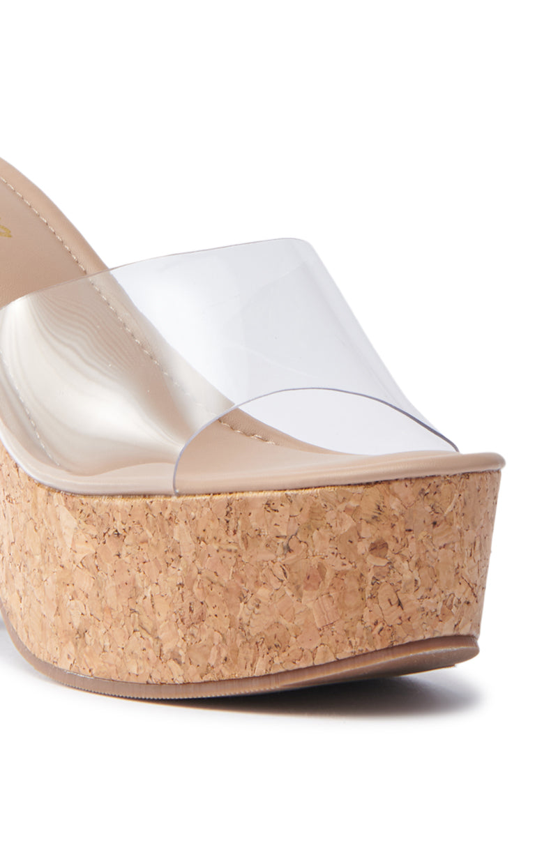 The DIEGO CORK WEDGE SANDAL features a close-up of its chunky cork heel and a wide clear PVC foot band. The tan insole contrasts with the cork and transparent strap, creating a chic, versatile look.