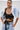 A woman with slicked-back hair models the DION BOLERO IN DENIM, a dramatic cropped jacket with puff sleeves, styled with a black lace bralette and high-waisted acid-wash jeans, standing against a plain white background.