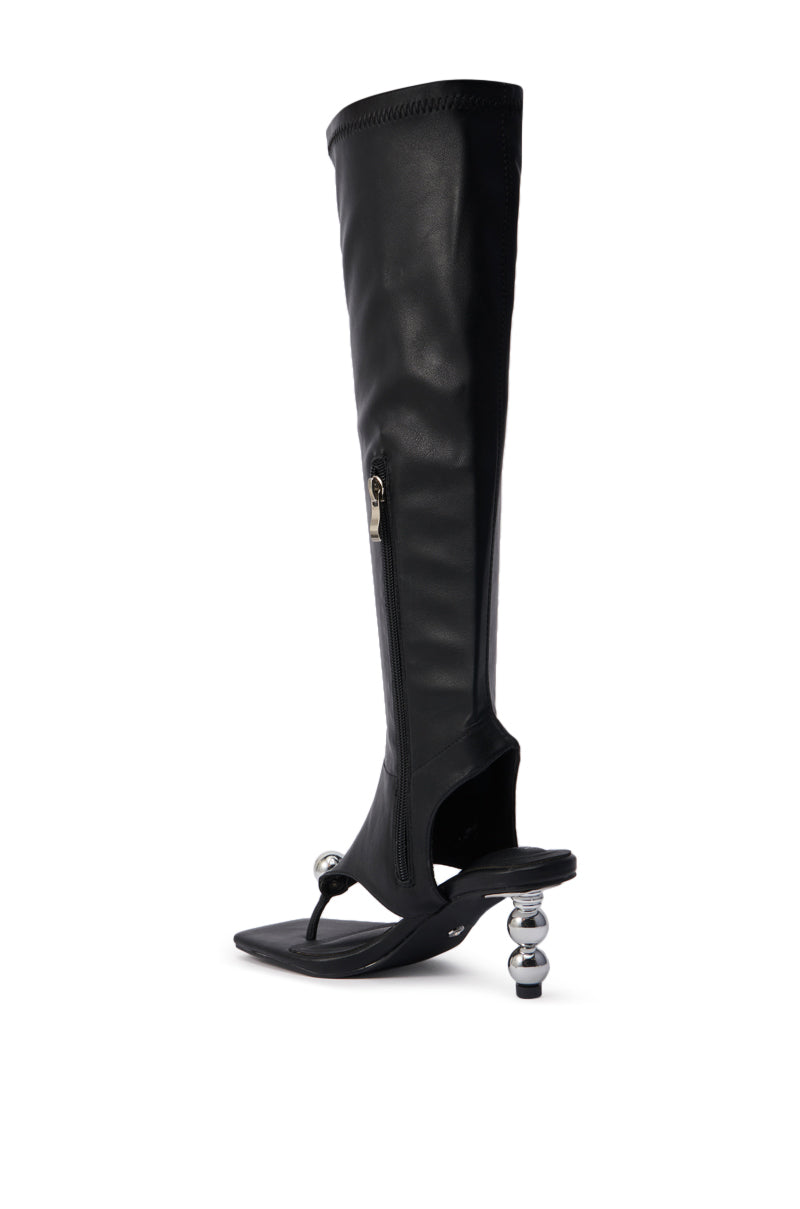 The AZALEA WANG DIPPIN DOT BLACK STRETCH SANDAL BOOT is a black faux leather knee-high sandal boot with an open square toe, thong design, side zipper, and a sculptural heel featuring metallic sphere accents.