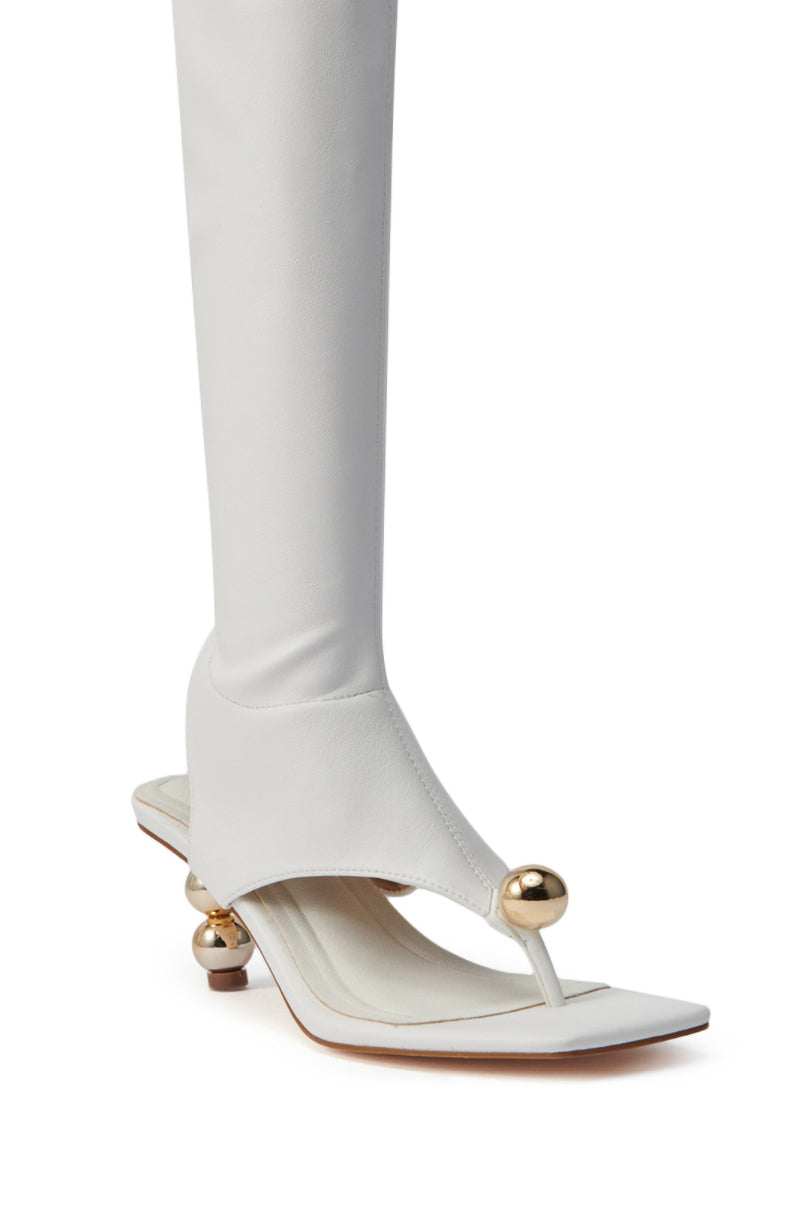 The AZALEA WANG DIPPIN DOT WHITE STRETCH SANDAL BOOT is a high-fashion faux leather knee-high with sculptural gold orb heels, square toe, unique foot and ankle coverage, and gold strap accents. Modeled on a white background.
