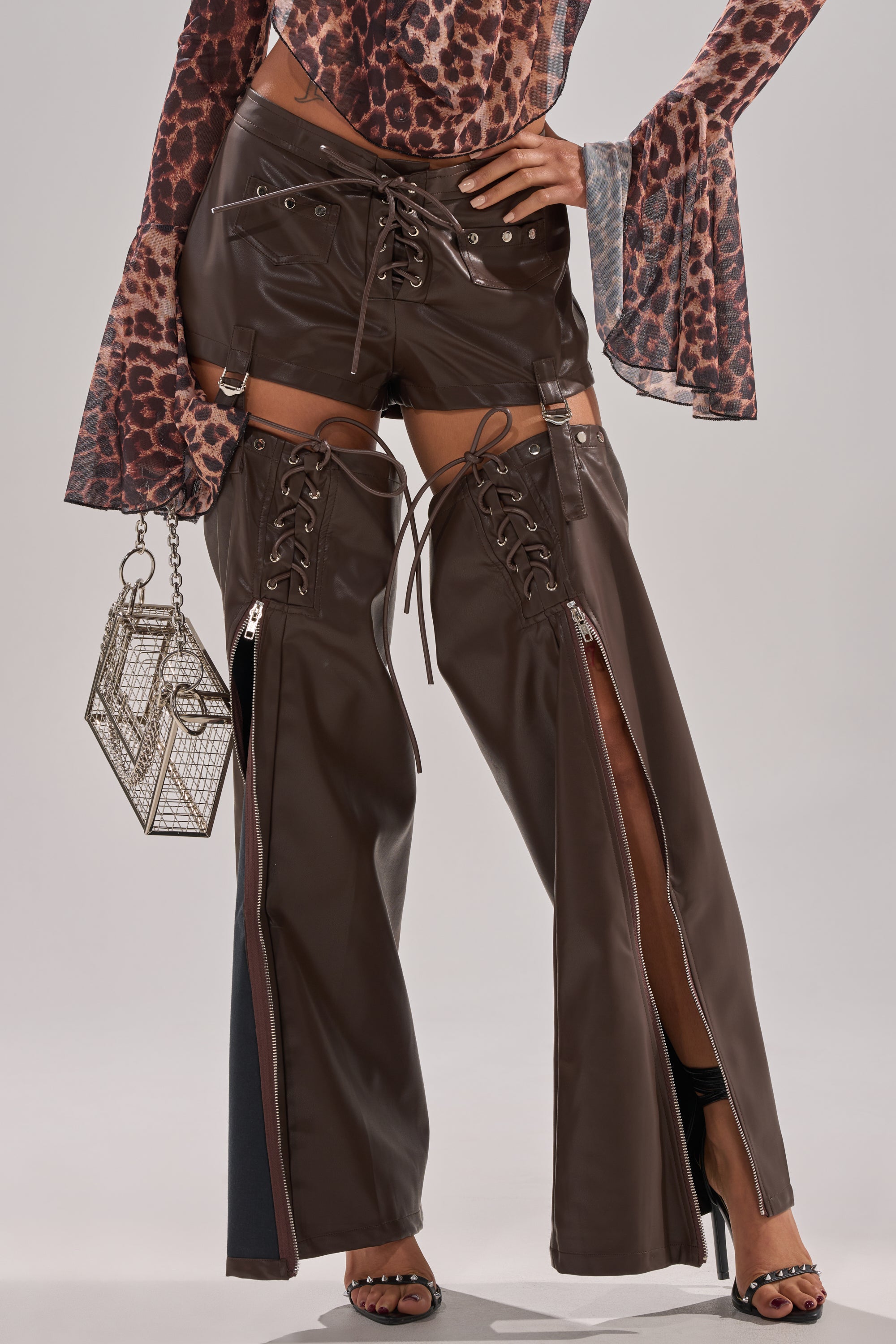 Wearing WANNA BE FAUX LEATHER CHAPS with thigh-high zippers, a leopard-print flared-sleeve top, black open-toe heels, and a geometric metallic mini handbag for a bold festival-ready look.