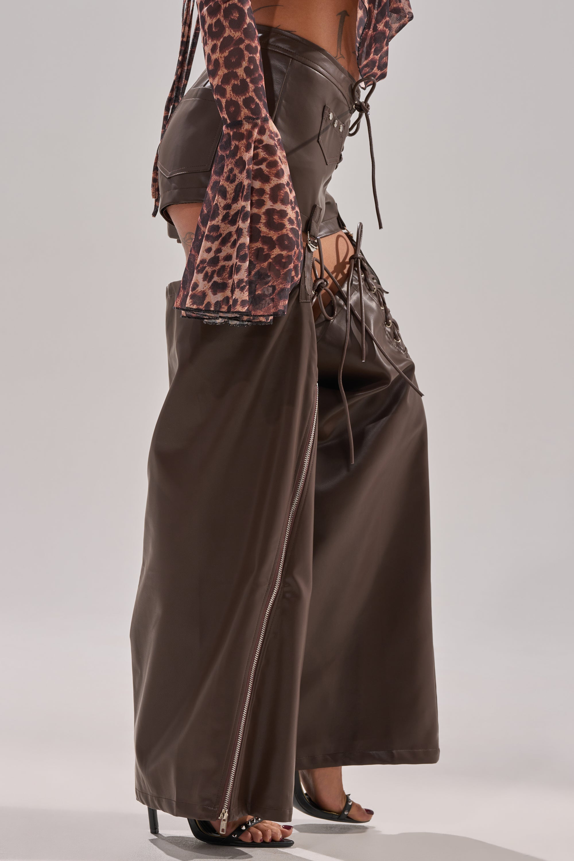 Wearing WANNA BE FAUX LEATHER CHAPS with side laces over matching Western-style shorts and an animal-print crop top, topped off with high-heeled sandals—a bold, festival-ready look.