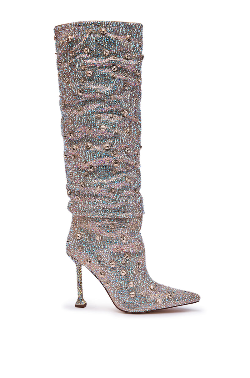 The AZALEA WANG DOUGHTY GOLD STILETTO BOOT is a tall, slouchy knee-high boot with a pointed toe and high heel, covered in gleaming rhinestones and beads, sparkling brilliantly against a white background.