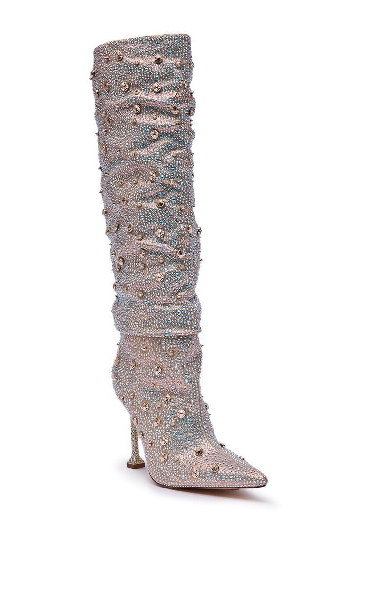 The AZALEA WANG DOUGHTY GOLD STILETTO BOOT is a tall, slouchy knee-high boot with a pointed toe, covered in sparkling rhinestones and embellished with round, jewel-like accents, displayed on a white background.