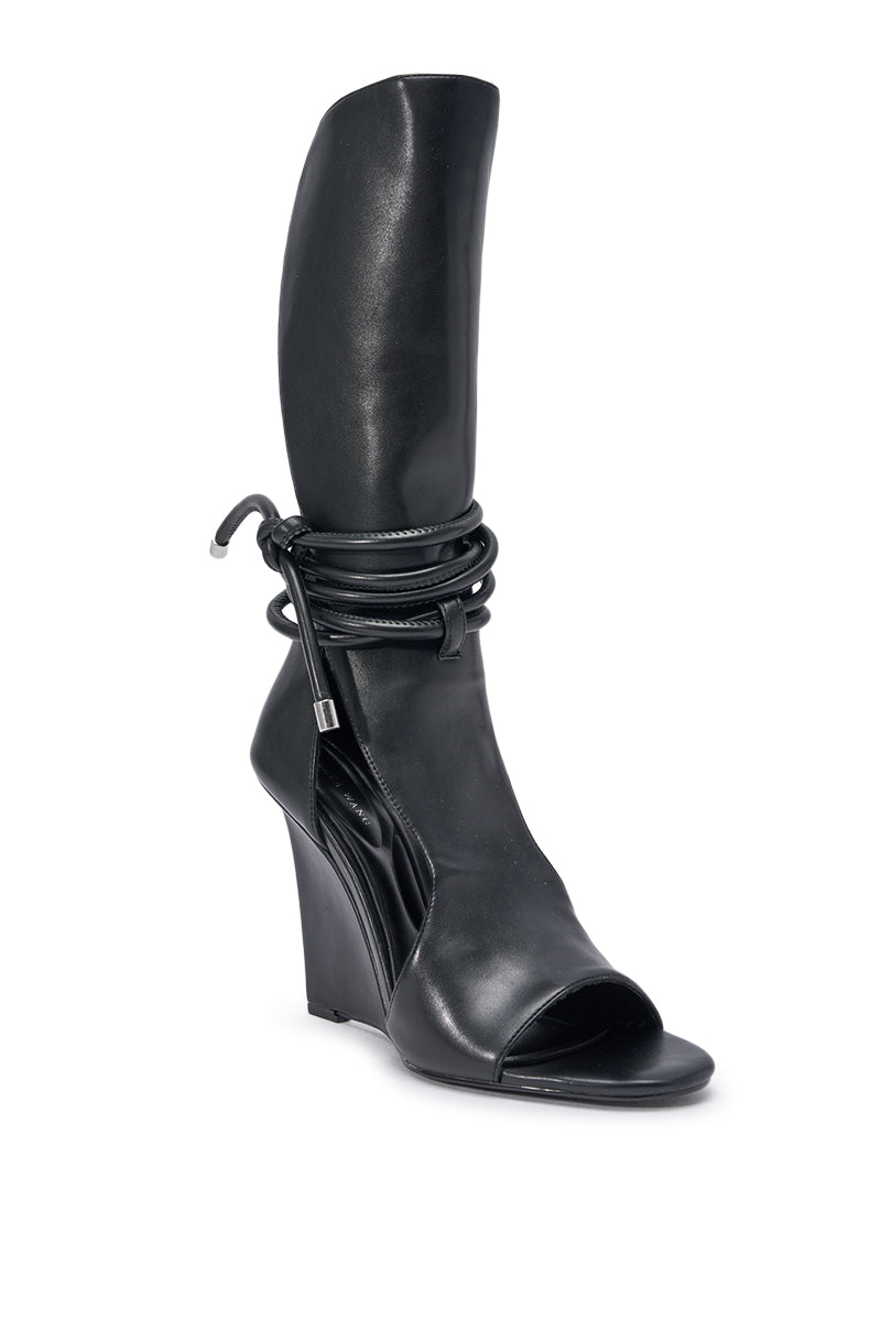The AZALEA WANG DOUMA is a black tall shaft wedge sandal with an open toe, curved design, and wraparound lace-up detail with metallic tips near the ankle. 3