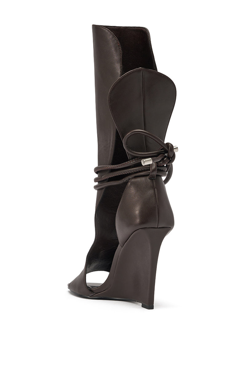 The AZALEA WANG DOUMA CHOCOLATE WEDGE LACE UP TALL SHAFT SANDAL is a dark brown faux leather sandal featuring a wedge heel, closed pointed toe, open sides, tall shaft, and wrap-around lacing tied at the back. 5