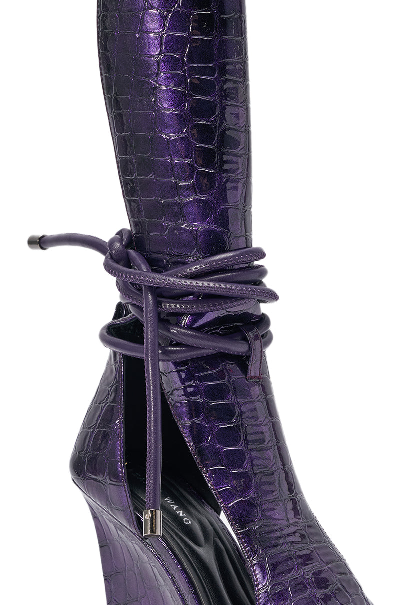A close-up of the AZALEA WANG DOUMA PURPLE CROC WEDGE SANDAL featuring a shiny purple croc-embossed finish, wedge heel, pointed toe, and wraparound ankle ties secured in a stylish bow. 5