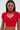 A woman wears the HEART YOU TEE IN RED, a fitted red crop top with short sleeves and a rhinestone-outlined heart cutout at the chest. She styles it with long straight hair and large hoop earrings.