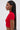 A woman with straight, long dark hair models the HEART YOU TEE IN RED—a fitted, short-sleeve cropped sweater with a heart-shaped cut-out—paired with large hoop earrings, shown in profile against a plain light background.