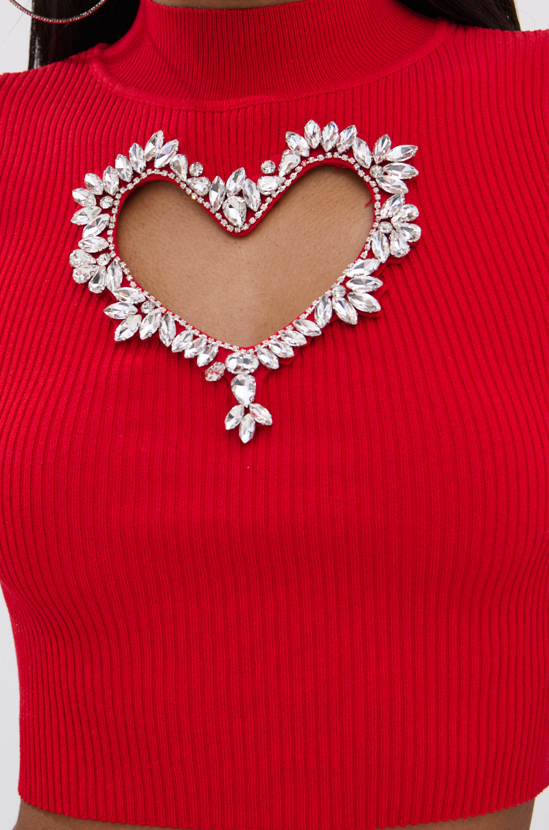 Close-up of the HEART YOU TEE IN RED, a ribbed cropped sweater with a heart-shaped chest cutout outlined in sparkling leaf-shaped rhinestones, modeled by a person with brown skin.