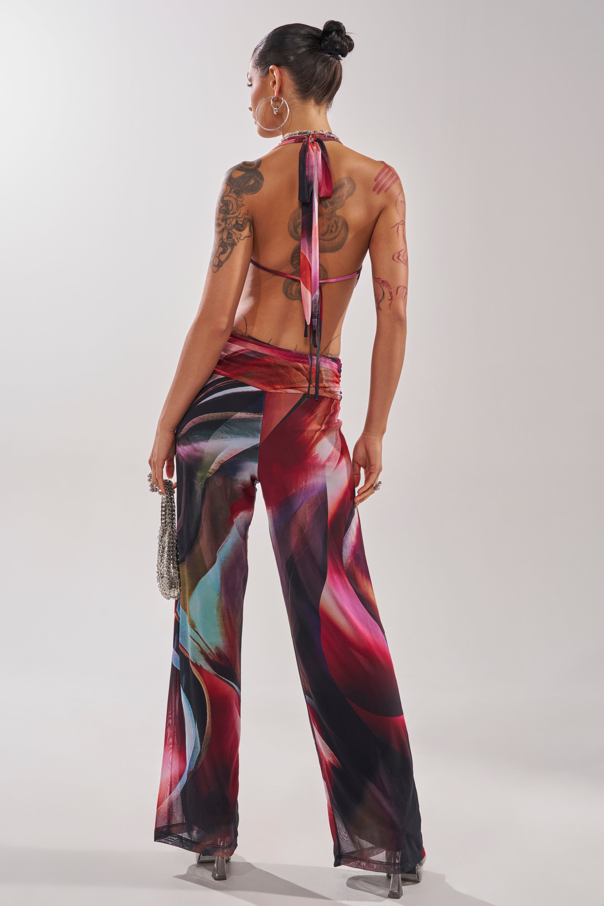 A woman in the MAIN CHARACTER ENERGY COWL NECK JUMPSUIT with a vibrant abstract print and halter neckline. 5