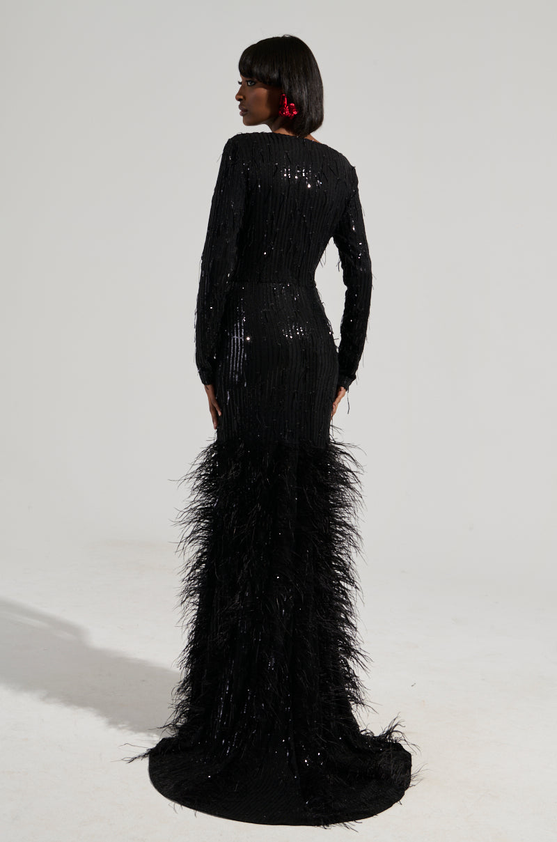 A woman in the YOURS TRULY Feather Sequin Embellished Maxi Dress, featuring a curve-hugging bodice, stands facing sideways. Her hair is styled in a bob, and she wears a red earring against a plain light-colored background.