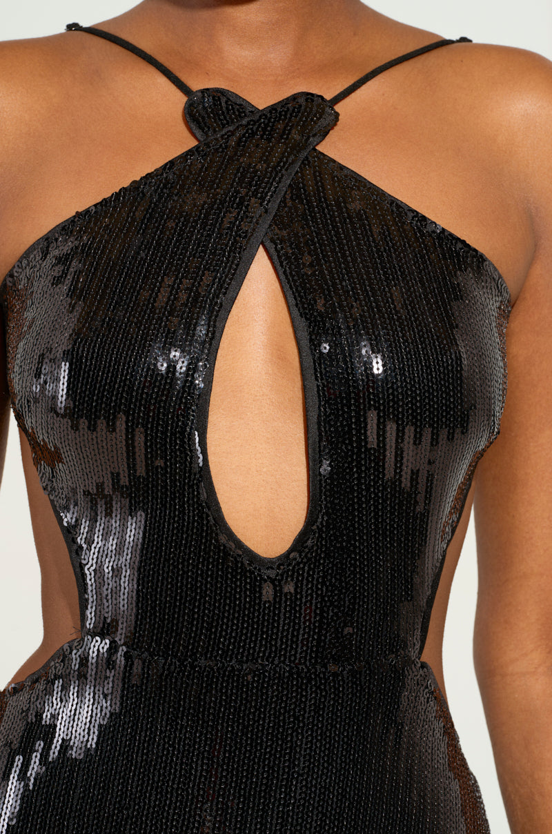 Close-up of a person wearing the ALL NIGHT LONG SEQUIN MAXI DRESS, featuring a halter neck, plunging neckline, and front keyhole cutout. The dress shimmers under the light, showcasing its glossy texture and intricate design.