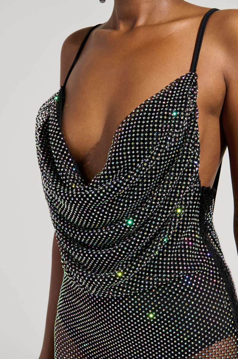 A person wearing the ACTIN BRAND NEW RHINESTONE MESH MAXI DRESS, featuring delicate thin straps and a cowl neckline. This sparkling attire showcases an intricate pattern that catches the light to produce a multicolored effect. The dress's plunging back enhances its allure, standing out against a neutral background to highlight its elegance.