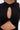 Close-up of a person in the NOT TOO CASUAL KNIT MAXI DRESS IN BLACK, a sleeveless maxi dress with a chest keyhole cutout and twisted fabric detail below, revealing part of the midriff.