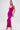 A woman stands against a white background wearing the ALWAYS ON THE MOVE RUCHED MIDI DRESS in bright fuchsia with a halter neck, ruched detail, side slit, and gold strappy high-heeled sandals.