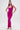 A woman poses confidently in the ALWAYS ON THE MOVE RUCHED MIDI DRESS, a bright pink halter-neck, bodycon midi with ruching. She pairs it with high-heeled sandals and wears her long straight hair in a high half-ponytail against a white background.