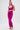 A woman poses against a white background wearing the ALWAYS ON THE MOVE RUCHED MIDI DRESS in bright pink and strappy high heels, her hair styled in a sleek ponytail.