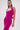 A woman with long, straight brown hair poses confidently against a plain light background wearing the ALWAYS ON THE MOVE RUCHED MIDI DRESS in bright pink and silver hoop earrings.