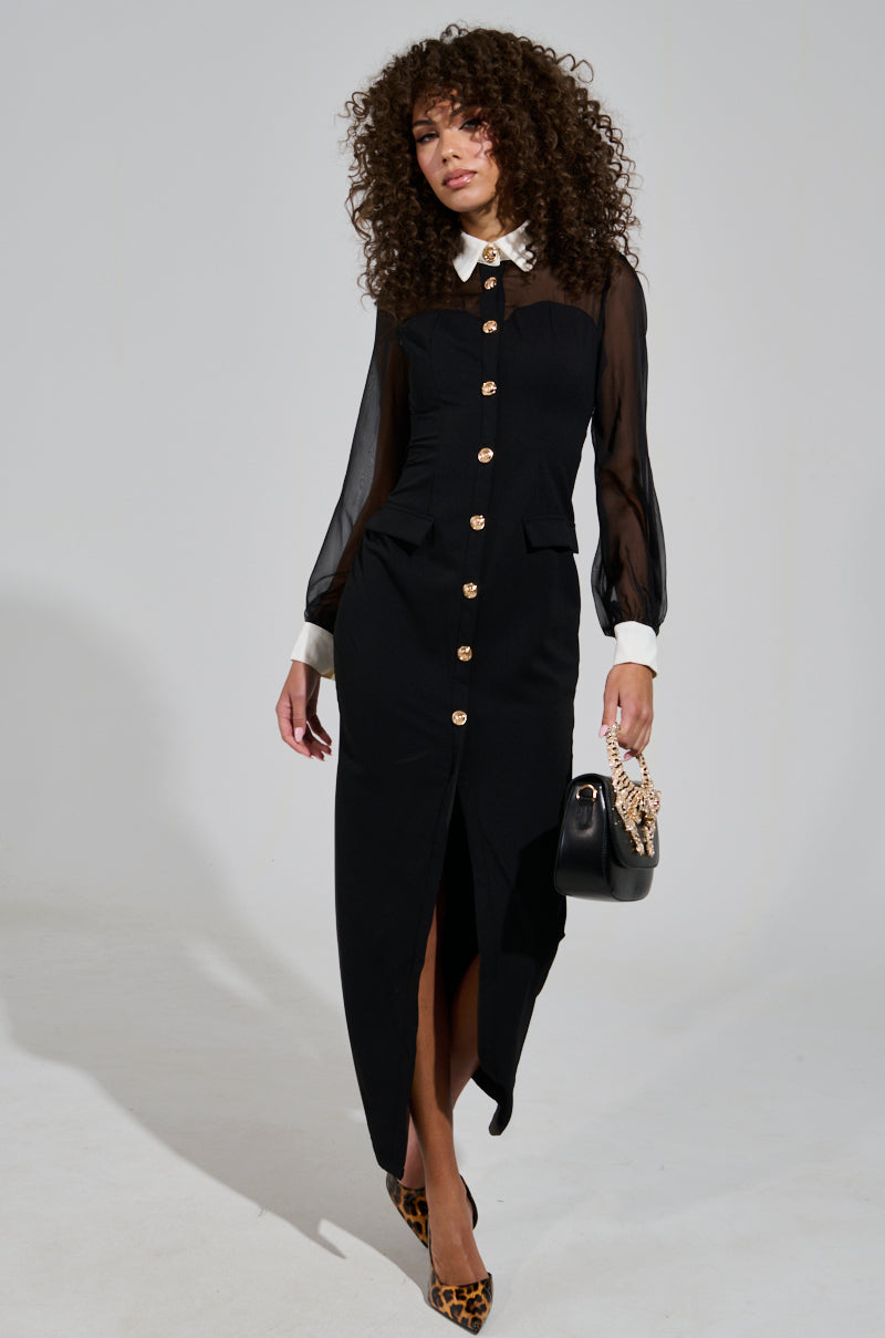 A person with curly hair wears the BUTTON UP BUTTER CUP COLLARED MAXI DRESS in black, featuring gold buttons and sheer mesh sleeves. They carry a handbag with ornate detailing and wear leopard-print shoes, standing against a plain background.