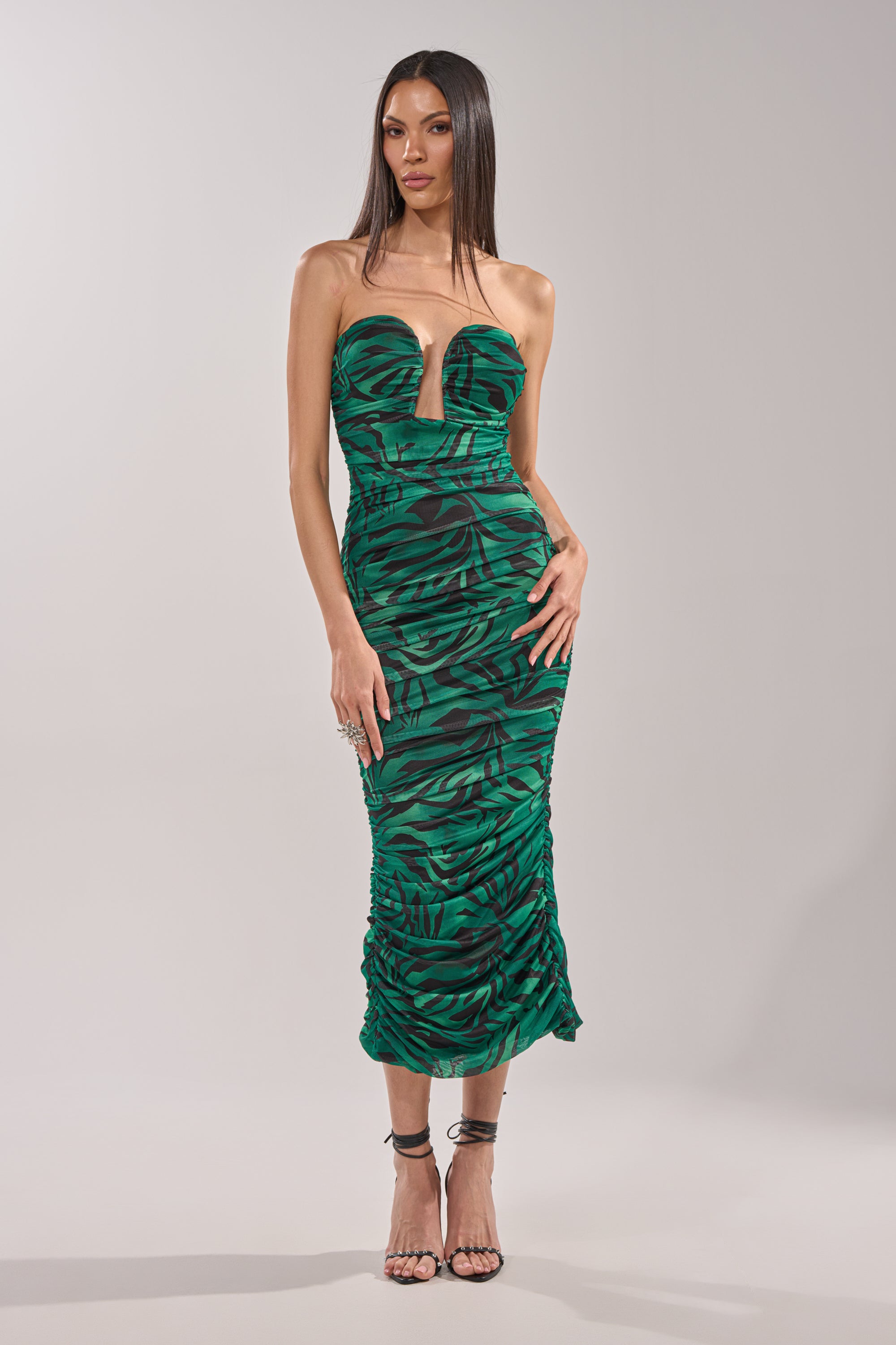 A woman wears the DAY OUT STRAPLESS PRINT MIDI DRESS, featuring a green zebra print and ruched detailing, styled with high-heeled sandals, standing against a plain background. 2