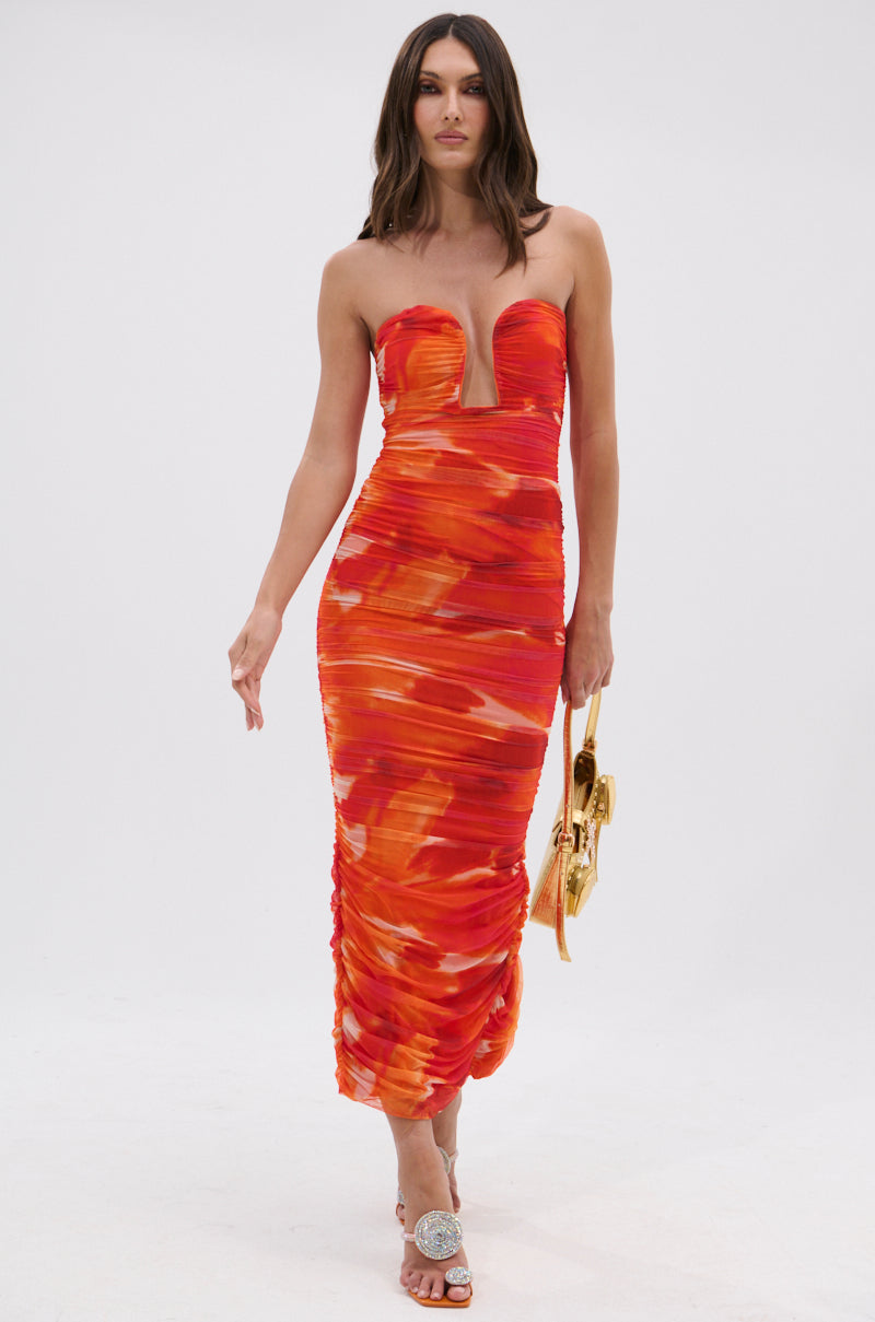 A woman in the LOTS OF LOVE OMBRE MIDI DRESS, with a strapless neckline and orange-red ombre pattern, walks forward holding a gold handbag and wearing embellished open-toed heels against a plain white background.