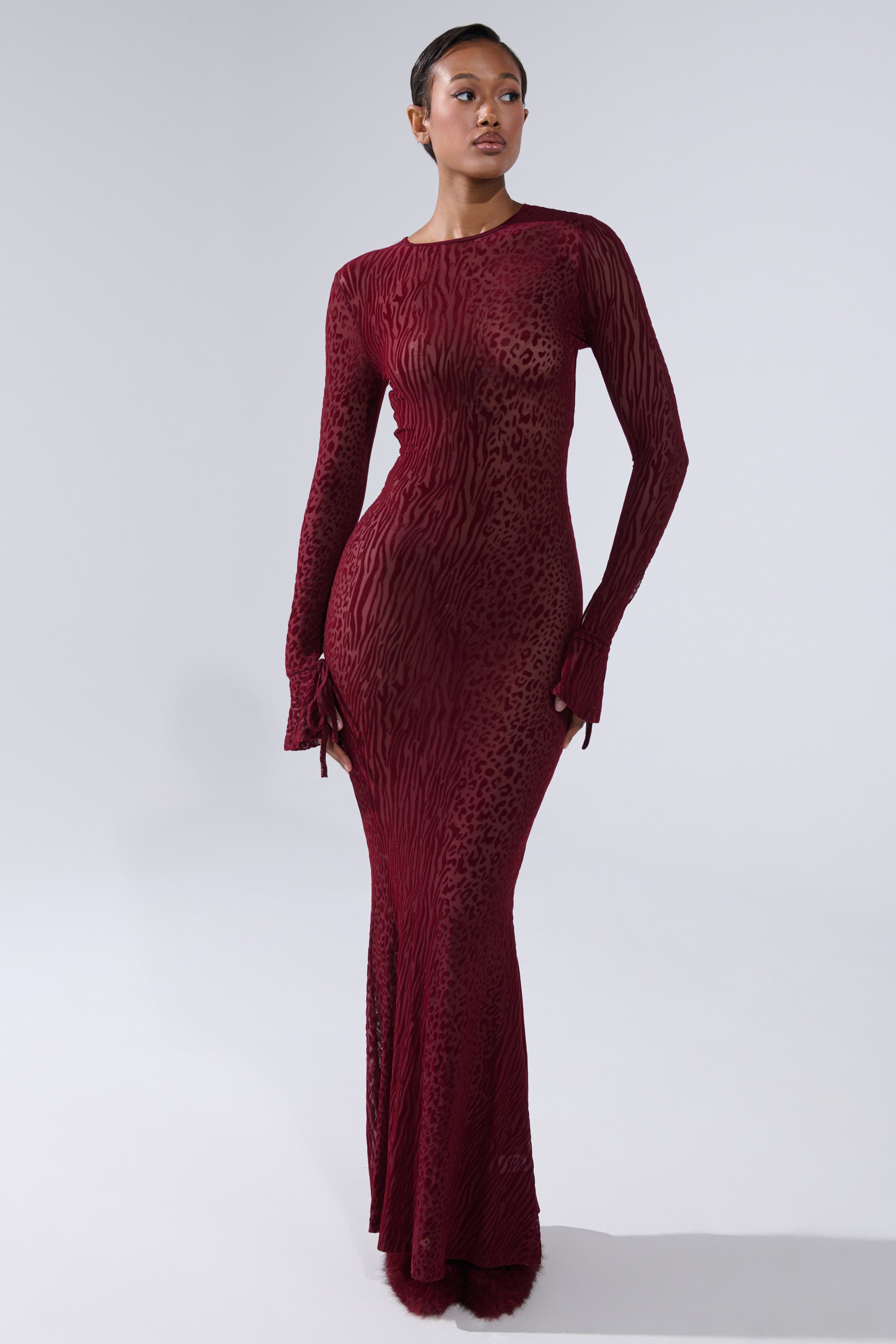 A woman stands against a light gray background wearing the MY GOOD SIDE Leopard Mesh Maxi Dress in Burgundy.
