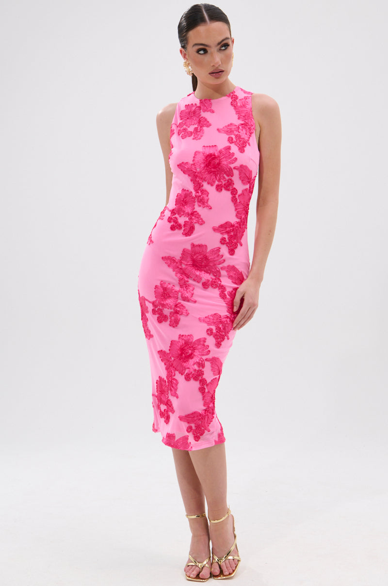 A woman poses against a white backdrop in the TIMELESS FLORAL MESH MIDI DRESS, featuring bold red floral appliqués. Her hair is slicked back, and she pairs the dress with gold strappy high-heeled sandals. 0