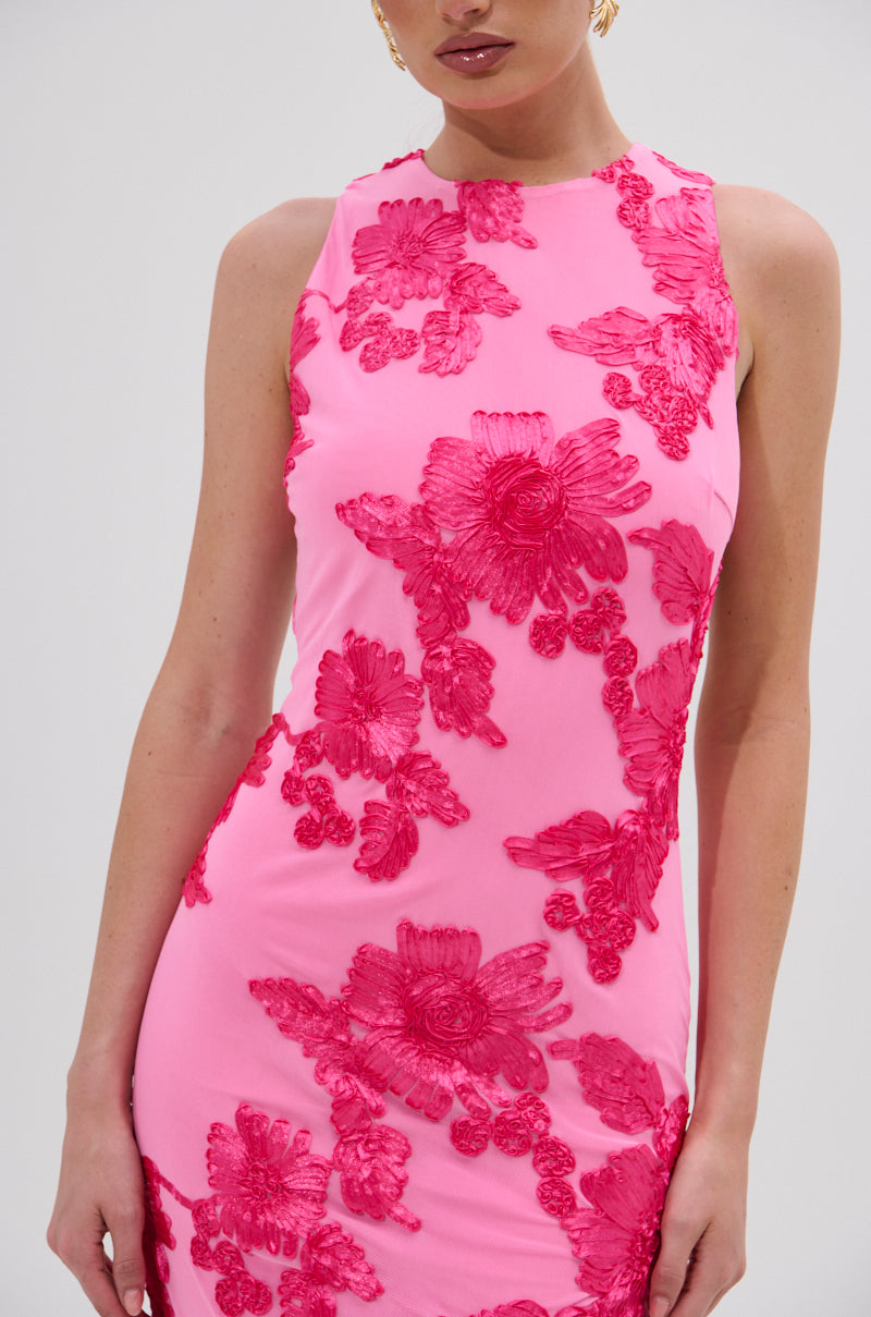 A woman in the TIMELESS FLORAL MESH MIDI DRESS, featuring a curve-hugging silhouette and bold hot pink floral appliqués, stands against a light background. 6