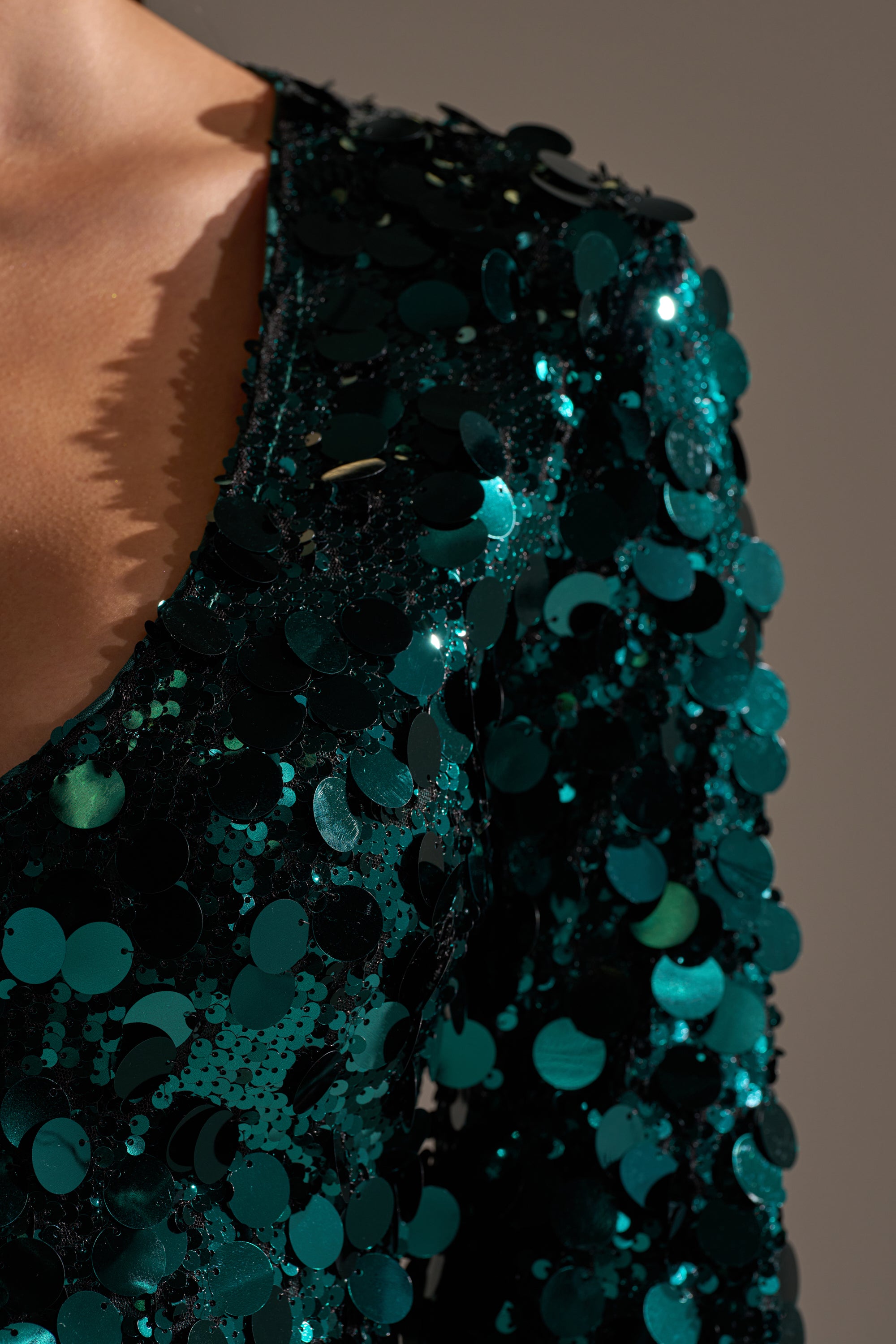 Close-up of a person wearing the DANCING QUEEN SEQUIN MINI DRESS, featuring shiny teal-green sequins, a plunging neckline, and long sleeves that create a bold and sparkling look as the sequins catch the light.