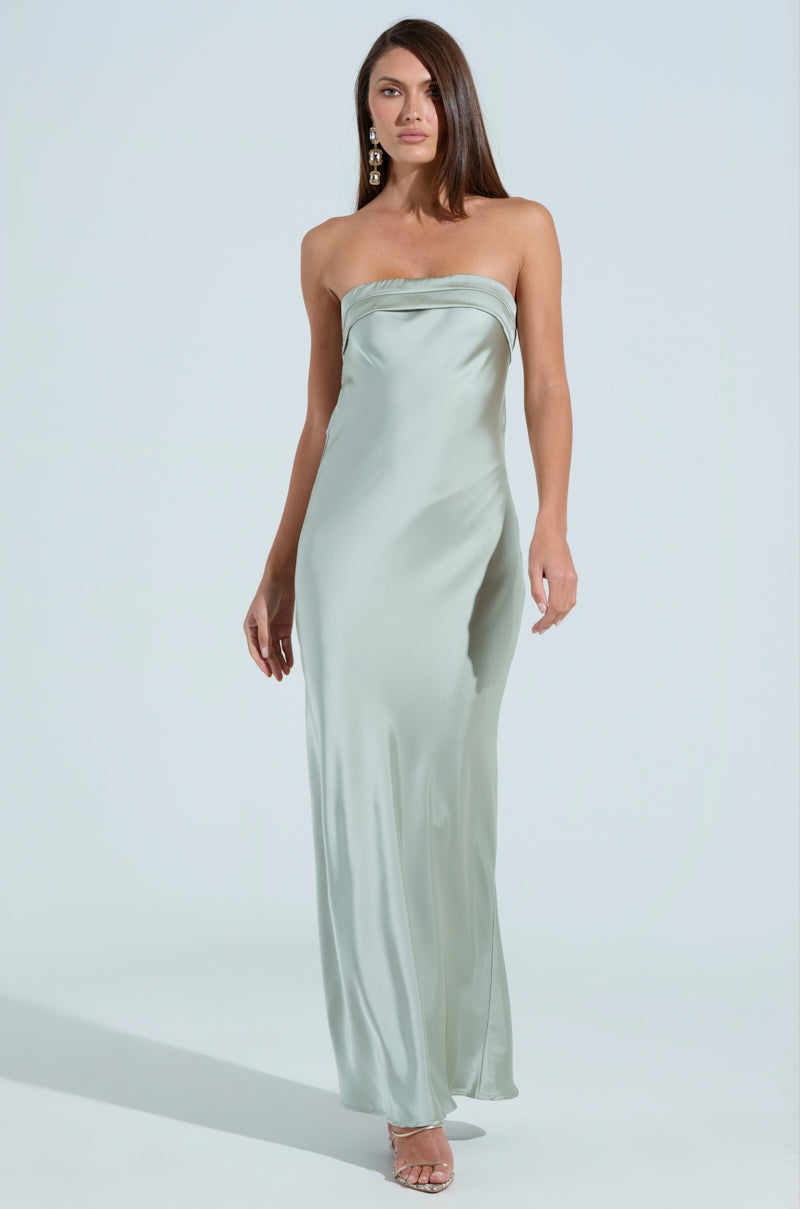 A woman poses confidently in the strapless, silky THE ONE THAT GOT AWAY SATIN MIDI DRESS, featuring a mermaid silhouette in light green. Her long, straight hair and large dangling earrings enhance the dress's elegant style against a plain background.