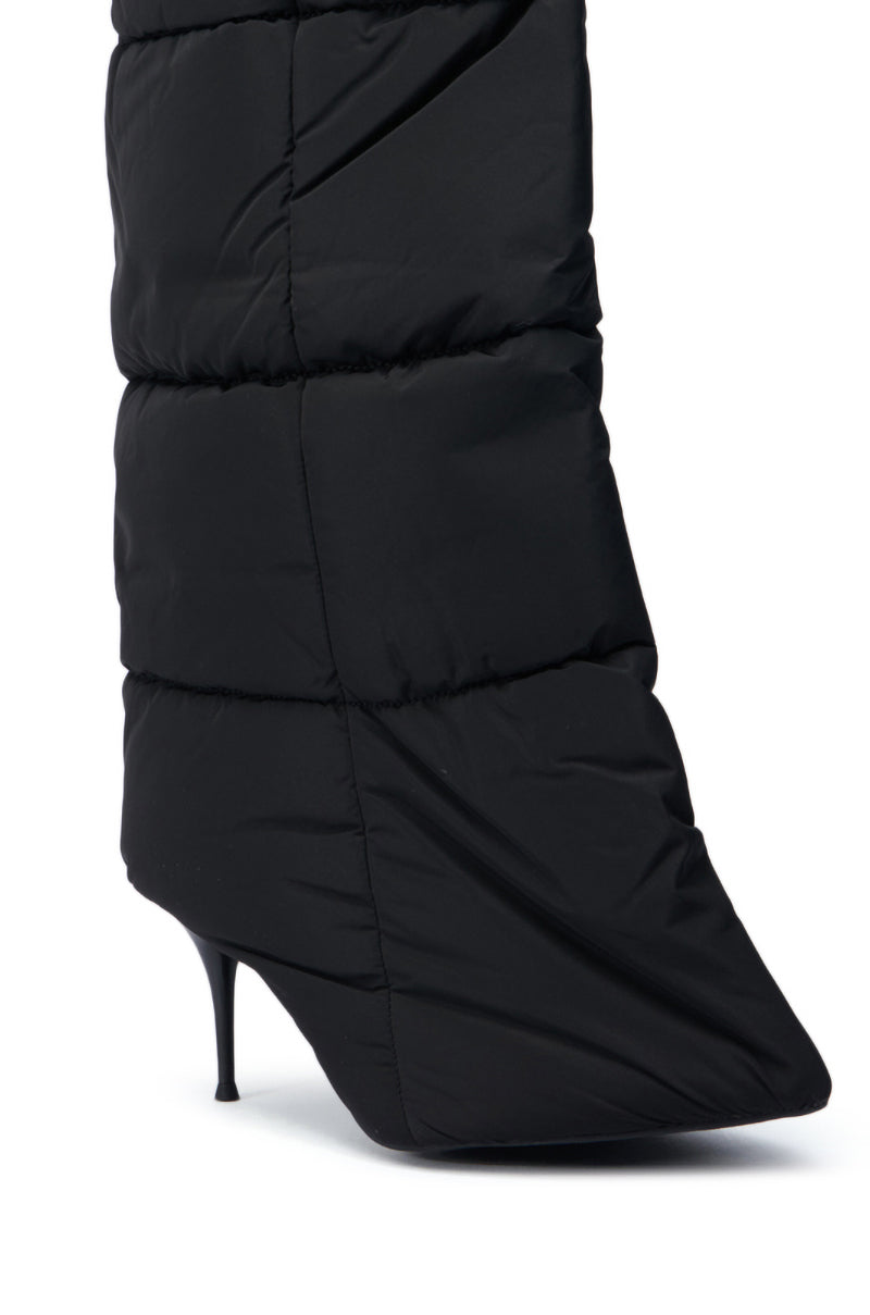 A close-up view of the DREAMSICLE BLACK PUFFER STILETTO BOOT showcases its high, thin heel and mid-calf shaft. The quilted upper features a puffy, insulated design reminiscent of a sleek puffer jacket with slightly shiny fabric.