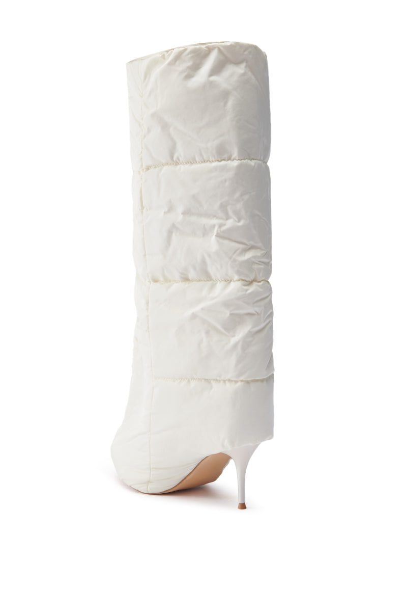 The DREAMSICLE CREAM PUFFER STILETTO BOOT is showcased against a simple white backdrop, highlighting its quilted design. With a pointed toe and slender high heel, it boasts a chic and modern sculptural silhouette.