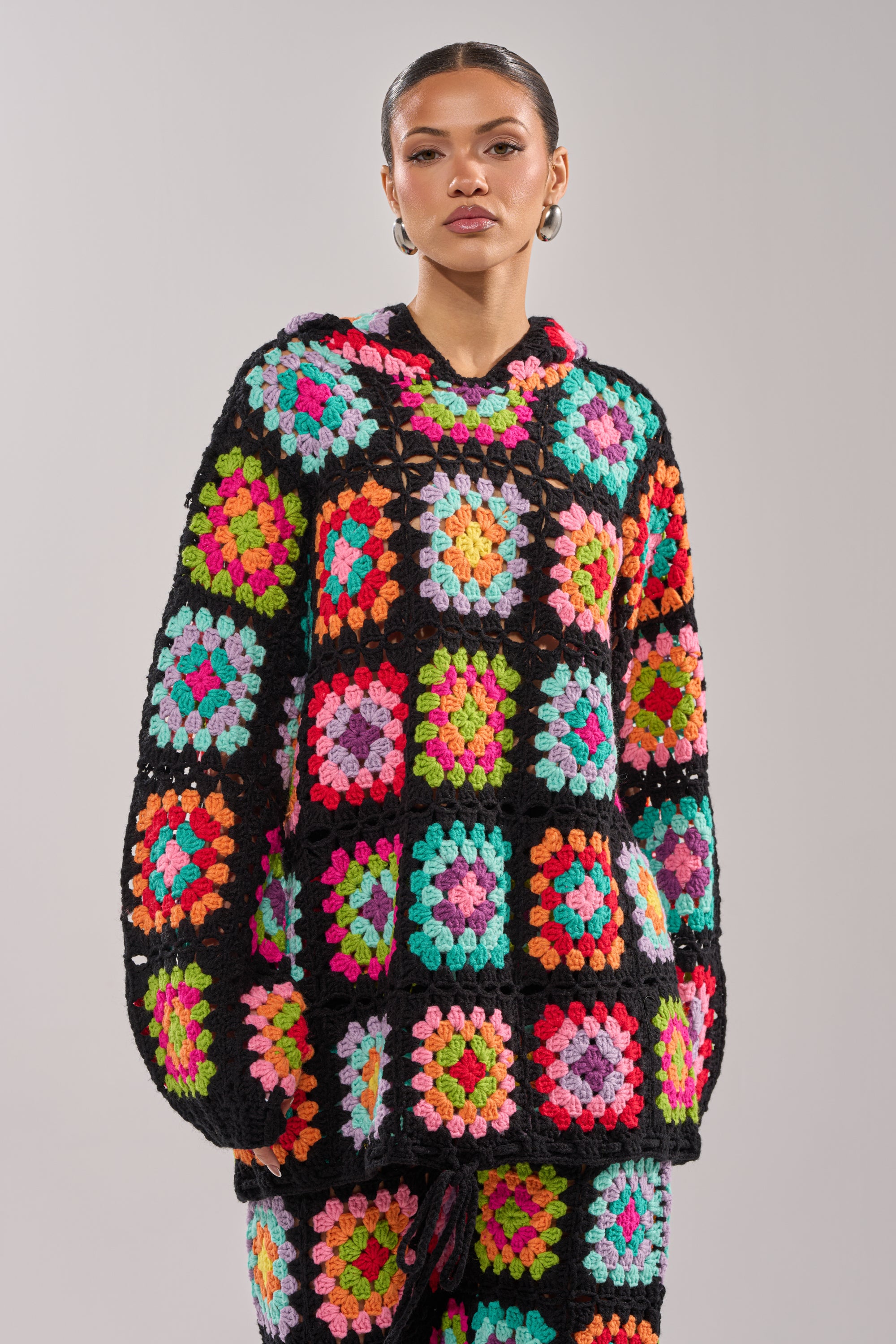 A person models the FESTIVAL GIRLY OVERSIZED CROCHET SWEATSHIRT IN MULTI, styled with matching pants, against a plain light grey background.