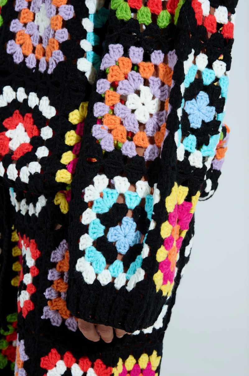 The AKIRA Label Festival Girly Oversized Crochet Sweatshirt features vibrant granny squares in purple, orange, pink, and blue outlined in black yarn, creating an intricate pattern.
