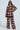 A person in large black sunglasses confidently showcases a vibrant AKIRA Label festival outfit. They wear a long-sleeve top paired with the Festival Girly Oversized Crochet Pant, featuring a square pattern adorned with red, blue, green, and white floral motifs.