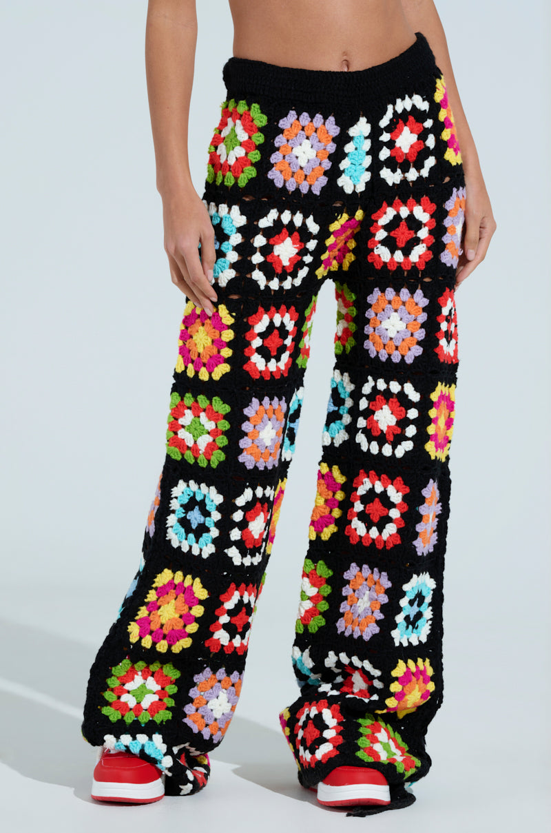 Sport the FESTIVAL GIRLY OVERSIZED CROCHET PANT, made of colorful granny squares in vibrant hues like red, orange, blue, and green against a plain background. Paired with red and white sneakers, this playful look radiates energy.