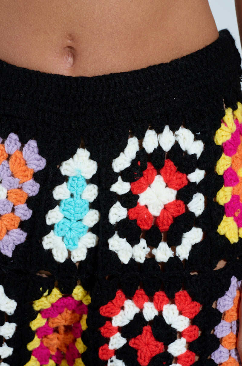 Close-up of someone's midsection wearing AKIRA Label's FESTIVAL GIRLY OVERSIZED CROCHET PANT. The vibrant crochet design includes red, white, black, purple, orange, and blue squares with skin visible at the top edge.
