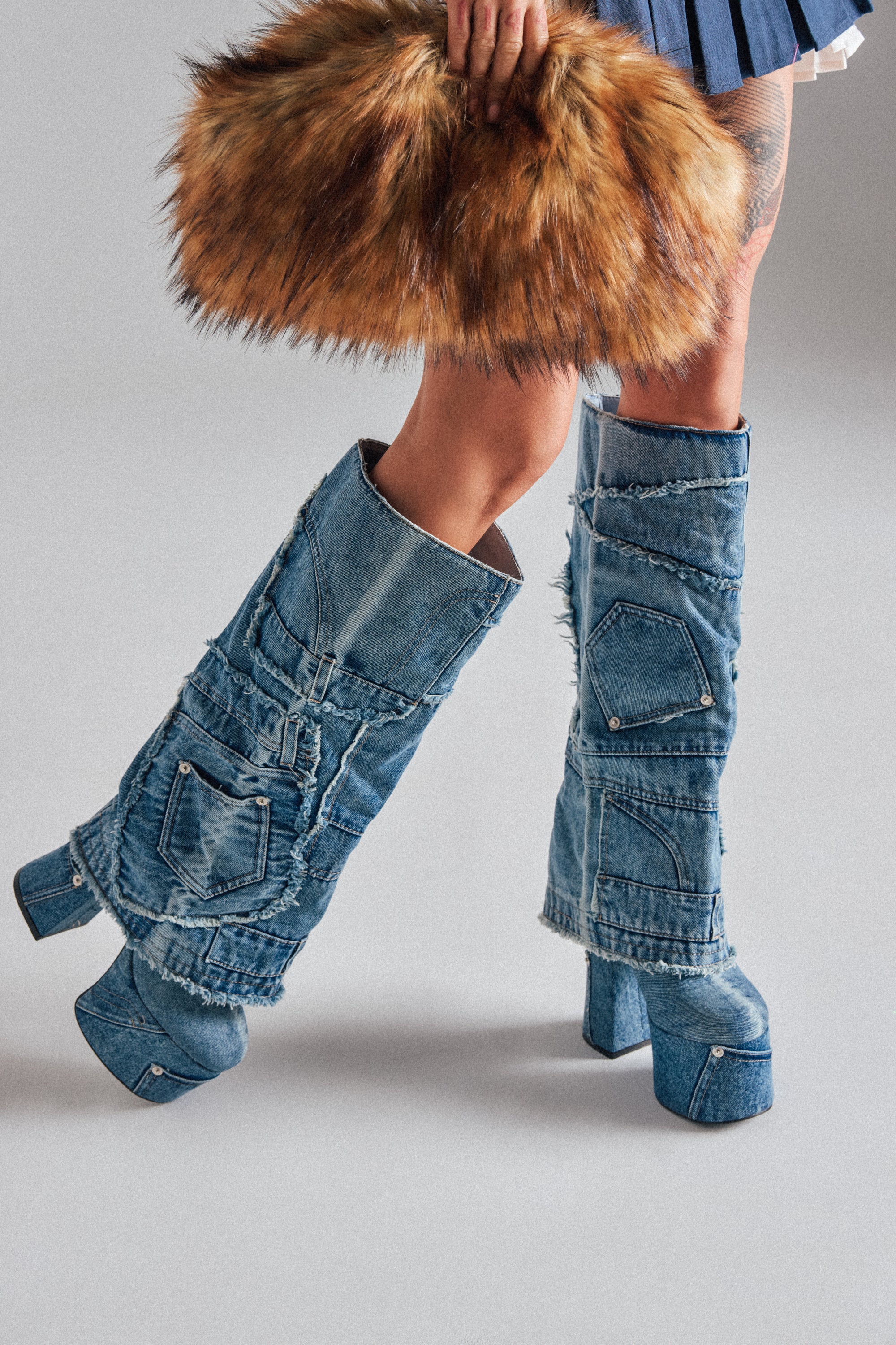 Wearing knee-high AZALEA WANG DUMI DENIM CHUNKY PATCHWORK BOOTS with a platform sole, holding a large fluffy brown faux fur bag, and pairing them with a short pleated skirt. 1