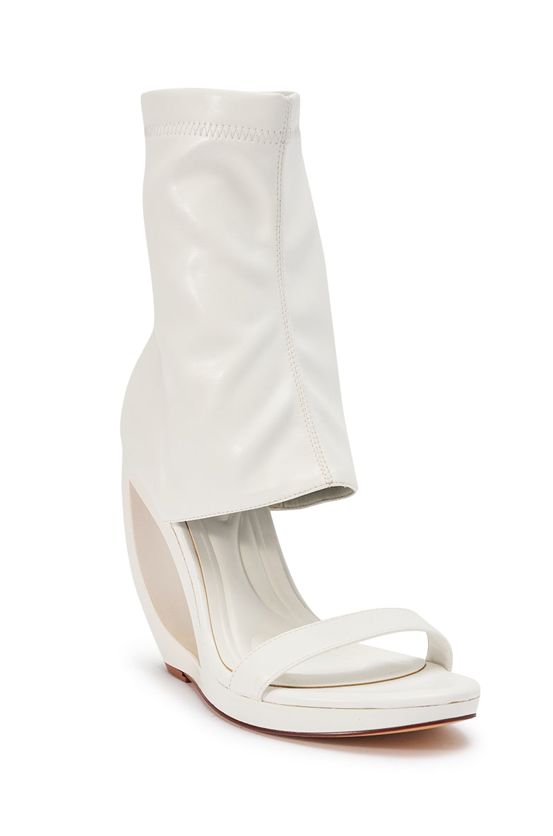 The AKIRA GOLD DUMISANI WHITE WEDGE OPEN TOE BOOTIE is a modern, smooth faux leather bootie with an open toe, distinctive curved wedge heel, and high sock-like ankle.