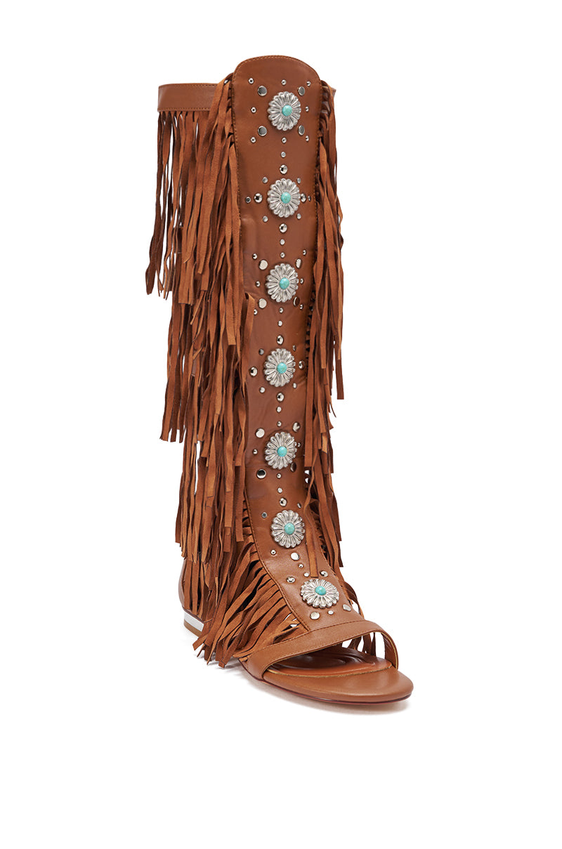 The AZALEA WANG DUSTINE BROWN GLADIATOR EMBELLISHED SANDAL is a tall, brown faux leather knee-high sandal boot featuring long fringe, turquoise concho accents, and silver studs running up the front. 5