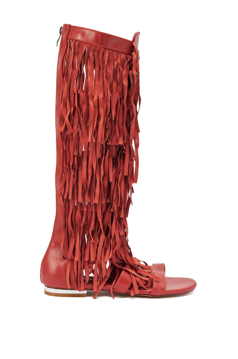 The AZALEA WANG DUSTINE RED MULTI GLADIATOR EMBELLISHED SANDAL is a knee-high, open-toe red sandal with layers of long vertical fringe strips covering the shaft, shown from the side against a white background. 2