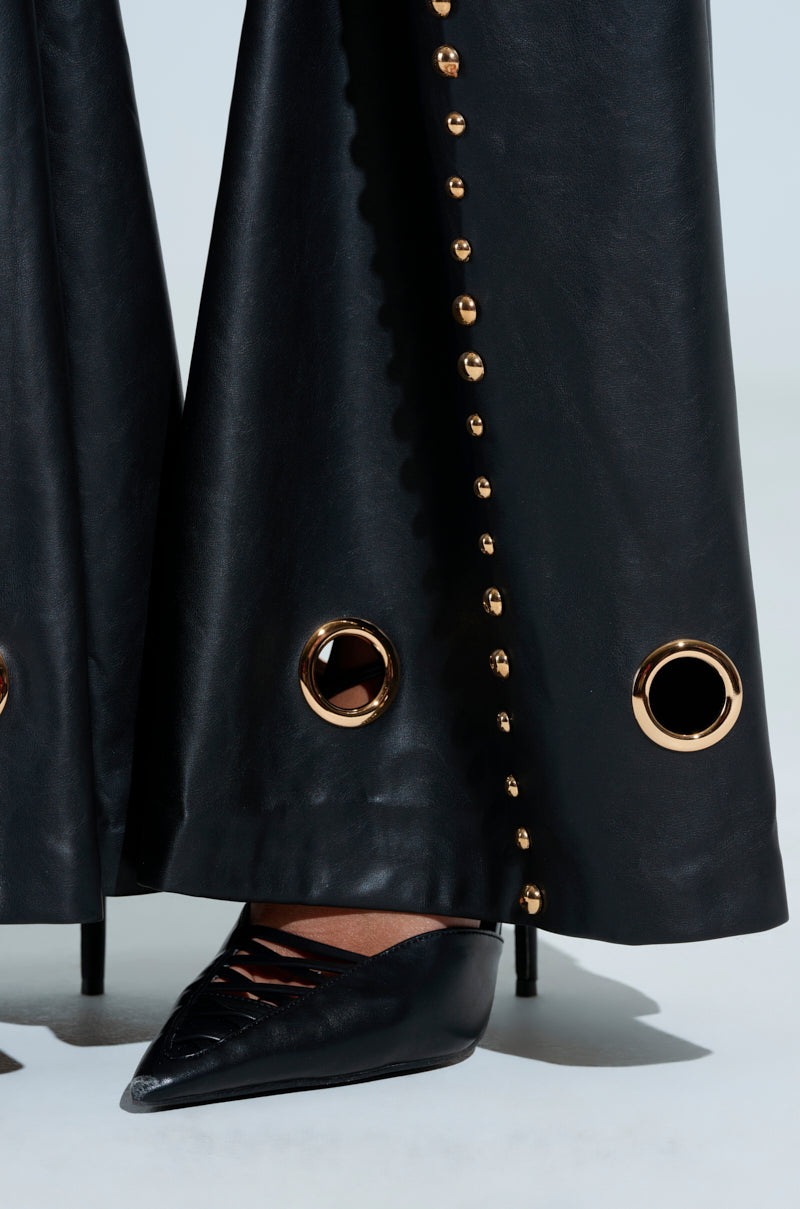 A close-up of DW STUDDED FLARE PANTS with gold embellishments and metallic studs near the hem, paired with black pointed-toe lace-up stilettos against a neutral background.