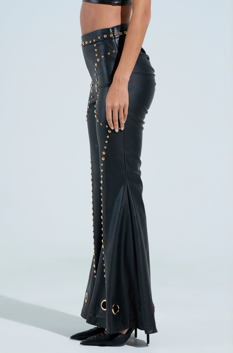 Someone wearing DW STUDDED FLARE PANTS with metallic stud detailing and grommets, paired with pointed black high heels. The pants have a modern design featuring a flared bottom and side detail.