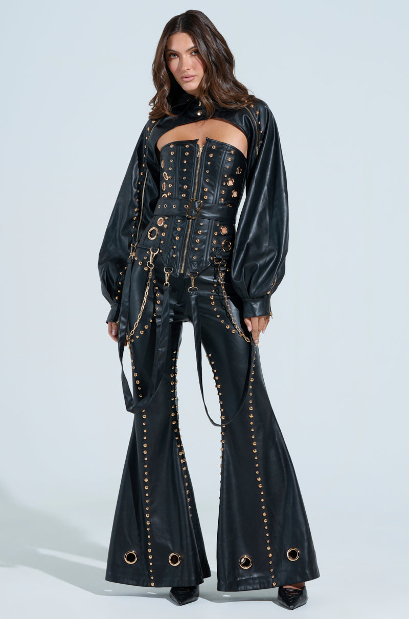 Someone is wearing the DW STUDDED FLARE PANTS set, consisting of a black leather corset top and high-rise flare pants with gold eyelet, metallic stud details, long sleeves, and chain accents on a plain light background.