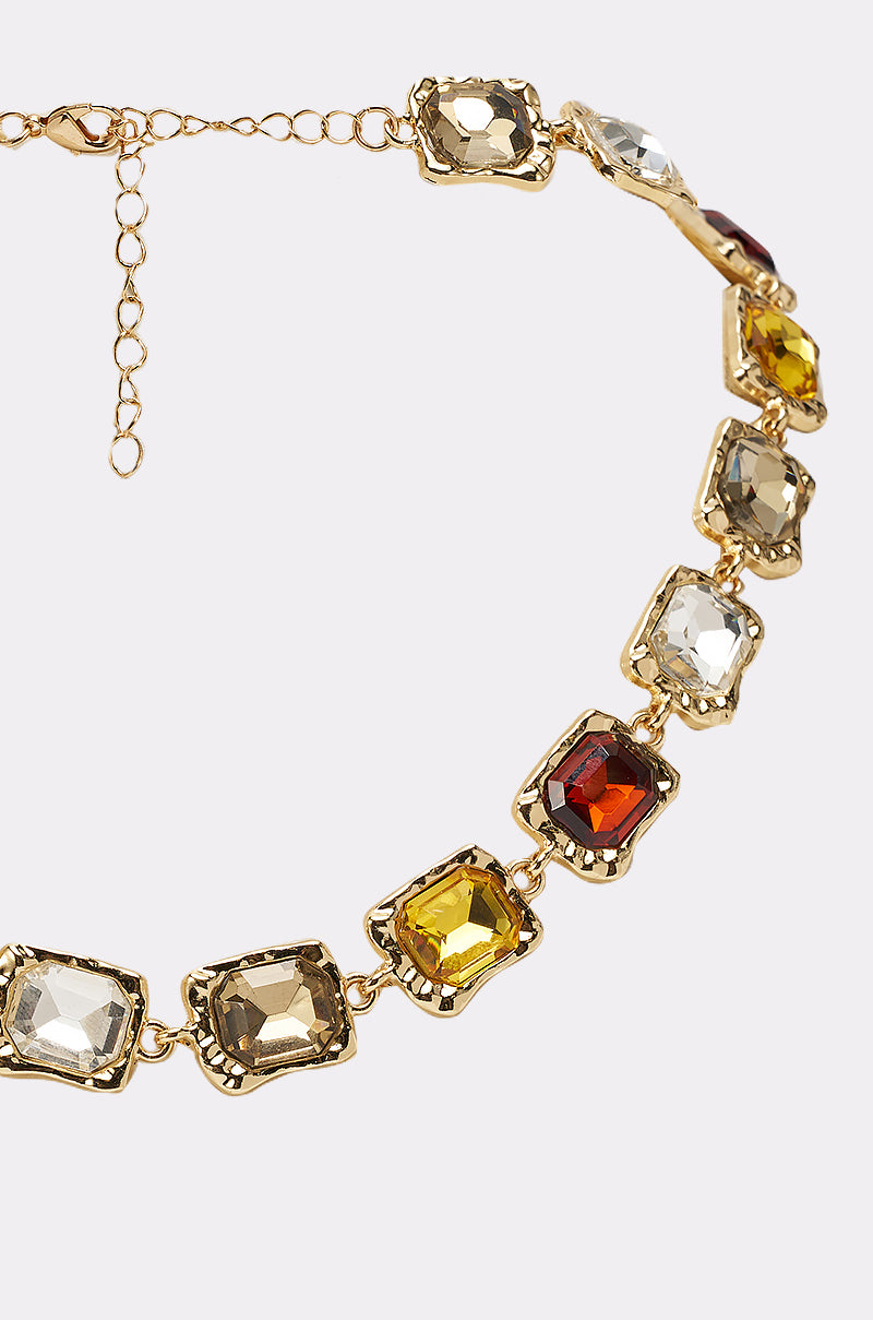 The STACK IT NECKLACE is a gold-tone statement piece showcasing large rectangular gemstones in clear, yellow, amber, and deep red set in ornate gold frames—perfect for evening wear. 2
