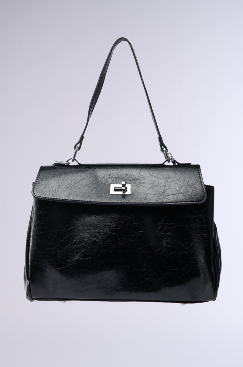 The ROXANNE FAUX LEATHER SATCHEL is a sleek black bag with a structured design and short handle. Its flap closure, featuring a silver rectangular buckle, contrasts elegantly against the light grey backdrop, while its textured faux leather enhances sophistication.