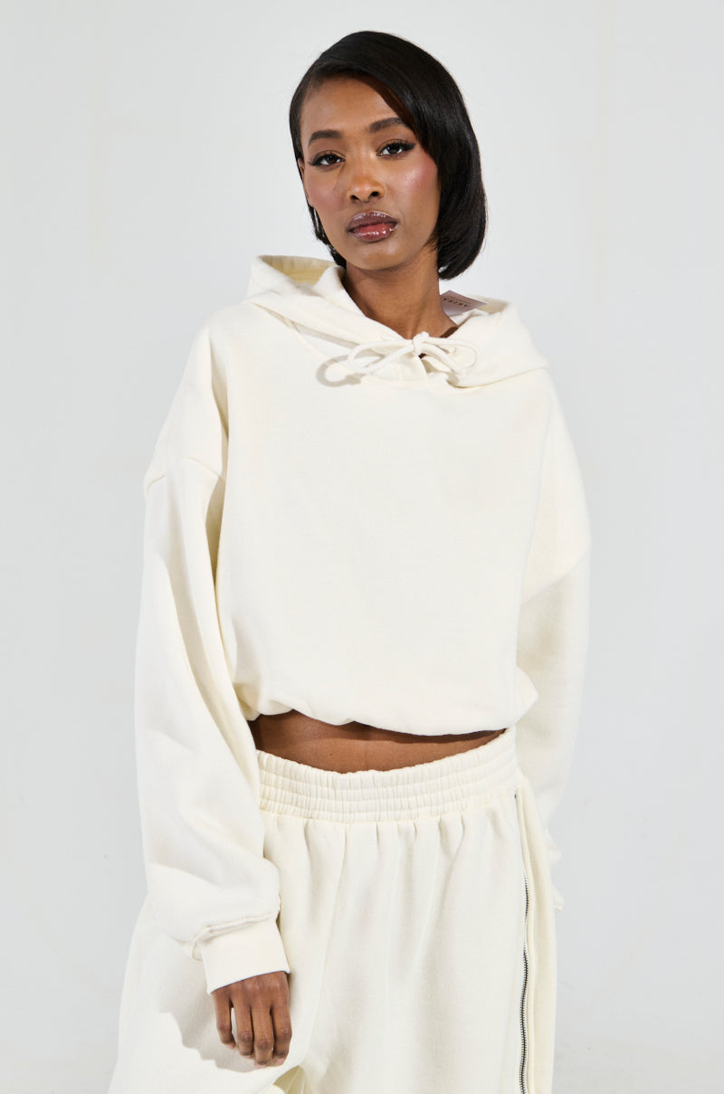 A person wearing the "AINT NOBODY SWEATSHIRT IN CREAM," made of a cotton blend, along with matching pants, stands against a plain background. They have shoulder-length dark hair and a confident expression. The loungewear sweatshirt is slightly cropped and features a drawstring at the neck for added style.