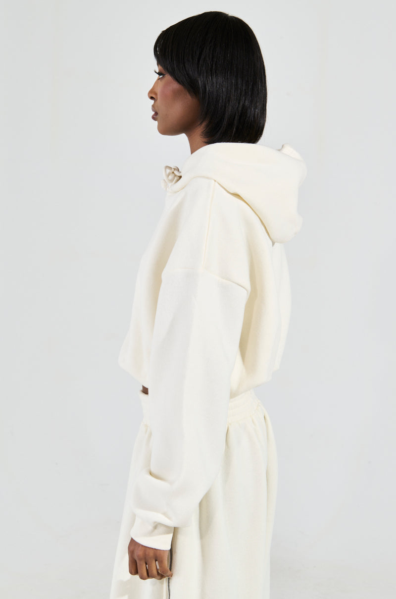 Side profile of a person wearing the AINT NOBODY SWEATSHIRT IN CREAM, made from a cotton-blend fabric, paired with matching loungewear pants. The cropped sweatshirt is styled to reveal a modern silhouette, beautifully complementing their short black hair against a plain light-colored background.